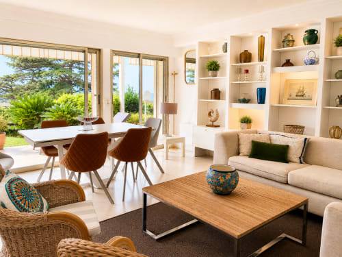Modern Cannes living room with beige sofa, wooden coffee table, white shelving, dining area, and garden views