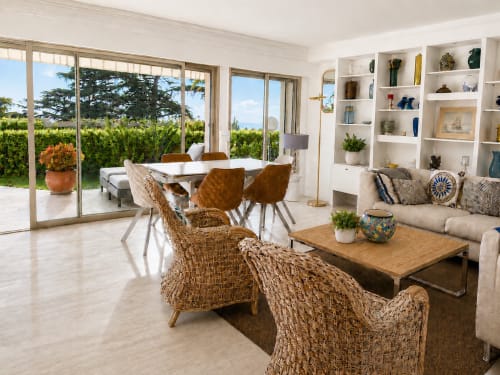 Bright Cannes villa interior with woven chairs, modern dining table, coastal views through glass doors, and built-in shelving