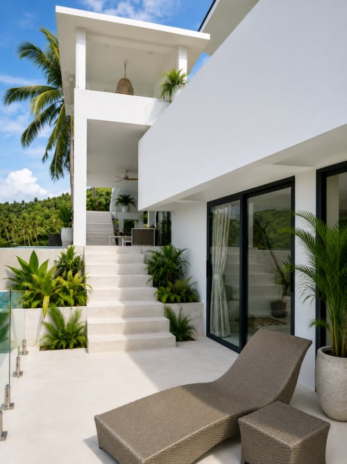 Modern white villa terrace in Ko Samui with lounge chairs, tropical plants, and palm trees overlooking gardens