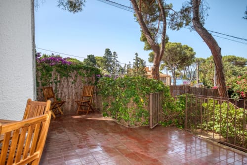 Terrasse avec chaises en bois, plantes grimpantes fleuries et pins à l'hôtel Finques Garcia Enrich à Palafrugell