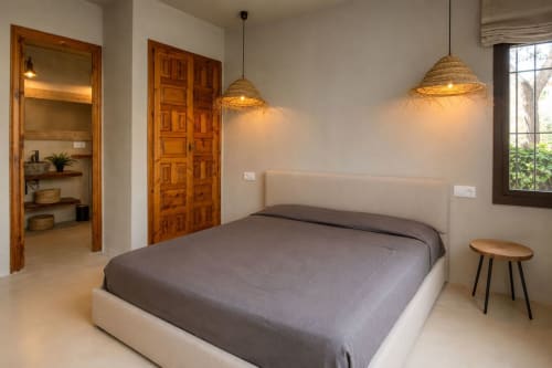 Chambre moderne aux Finques Garcia Enrich à Palafrugell avec luminaires en rotin tressé, lit crème et portes en bois.