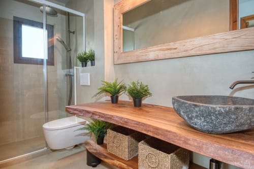 Baño moderno en Finques Garcia Enrich en Palafrugell con tocador de madera, lavamanos de piedra y ducha a ras de suelo