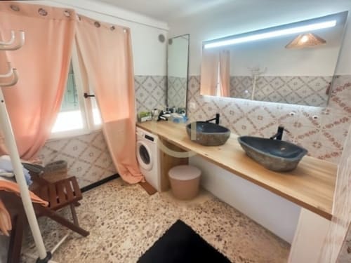 Salle de bains moderne avec deux vasques, plan de travail en bois, carrelage motifs et rideaux rose à Calvi