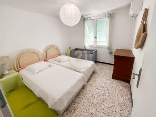 Chambre twin lumineuse dans un appartement à Calvi avec draps blancs, chaises tressées, climatisation et vue sur le jardin