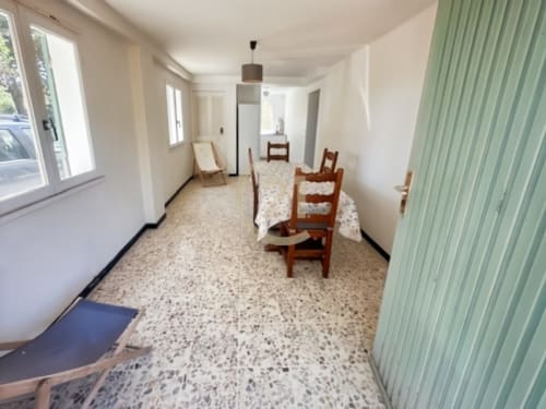 Couloir lumineux de l'appartement de Calvi avec sol en terrazzo, chaises en bois et mur d'accent vert offrant une vue sur le jardin