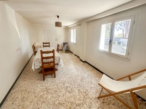 Salle à manger lumineuse avec chaises en bois, sol en terre cuite et portes vitrées donnant sur le jardin de l'appartement L'Île-Rousse