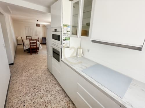 Cuisine moderne dans un appartement authentique à Calvi avec meubles blancs, double four et carrelage terrazzo menant à la salle à manger