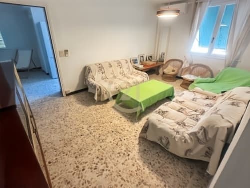 Spacieux séjour de l'appartement à Calvi avec plusieurs lits, table verte, chaises en rotin et lumière naturelle des fenêtres