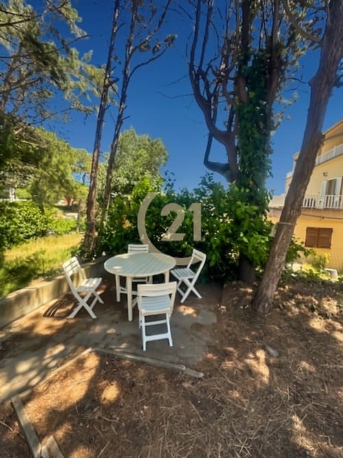 Terrasse ombragée avec ensemble de salle à manger blanc et grands arbres à l'appartement Calvi - Century 21 Dary