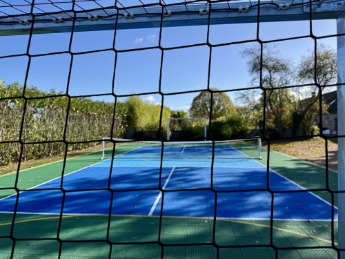 Terrain de pickleball professionnel aux surfaces bleue et verte à la villa HelloFamily de Montigny-le-Chartif, entouré d'arbres