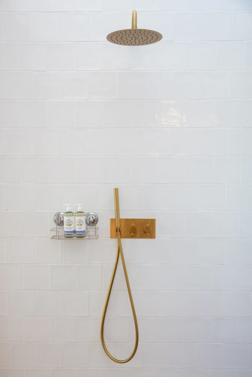 Modern bathroom shower setup with brass fixtures, rainfall showerhead, and white subway tile wall at Monte das Açoteias,