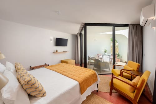 Bright Suite Mayor bedroom at Monte das Açoteias with pool view, yellow armchairs, and private terrace access in Tavira