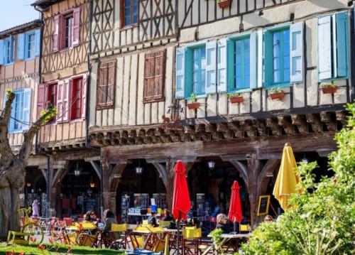 Maisons à colombages médiévales avec terrasse de café sous parasols rouges à Ferrières-sur-Ariège
