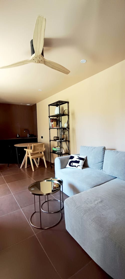 Salon moderne de la Domaine Alga B&B avec canapé bleu clair, ventilateur de plafond en bois et cuisine ouverte à Bourg-Charente