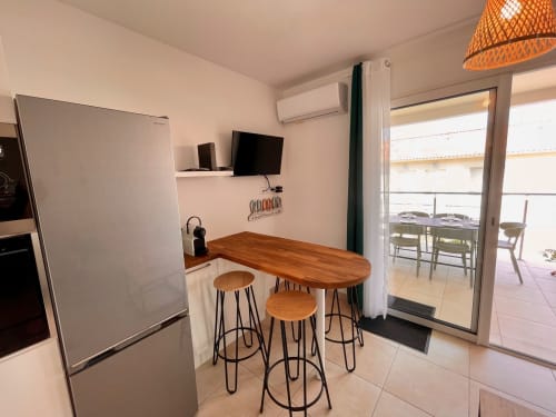 Angolo cucina moderno con bancone bar in legno, sgabelli, frigorifero, TV a parete e porte vetrate che si aprono su