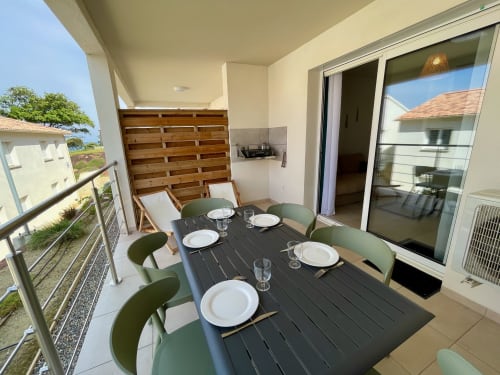 Modern beachside apartment terrace at Marina di Bravone with dining table, green chairs, and ocean views