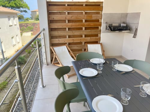 Beachfront apartment terrace at Résidence Marina di Bravone with dining table, green chairs, loungers, and grill setup