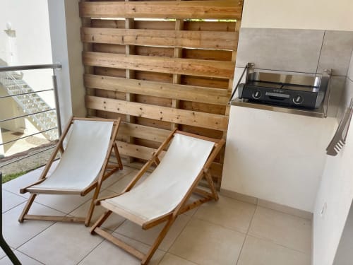 Wooden deck chairs with white cushions on a patio at Résidence Marina di Bravone beachfront apartment, with electric grill