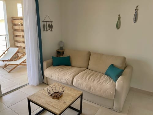 Beige sofa with teal pillows in Marina di Bravone apartment living room, wooden coffee table, beach access balcony view