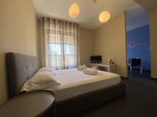 Modern bedroom at Cinelli Apartment in Vercelli with grey bed, pendant lights, yellow walls, and garden view curtains