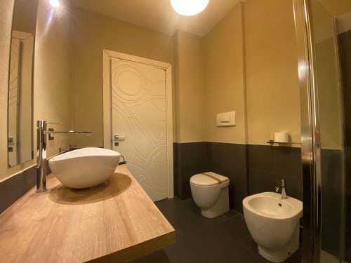 Modern bathroom at Cinelli Apartment in Vercelli with wood vanity, white vessel sink, bidet, toilet, and black tile accents