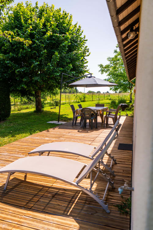 Terrasse ensoleillée de La Maison Du Saule avec chaises longues, parasol cantilever, table à manger et vue champêtre