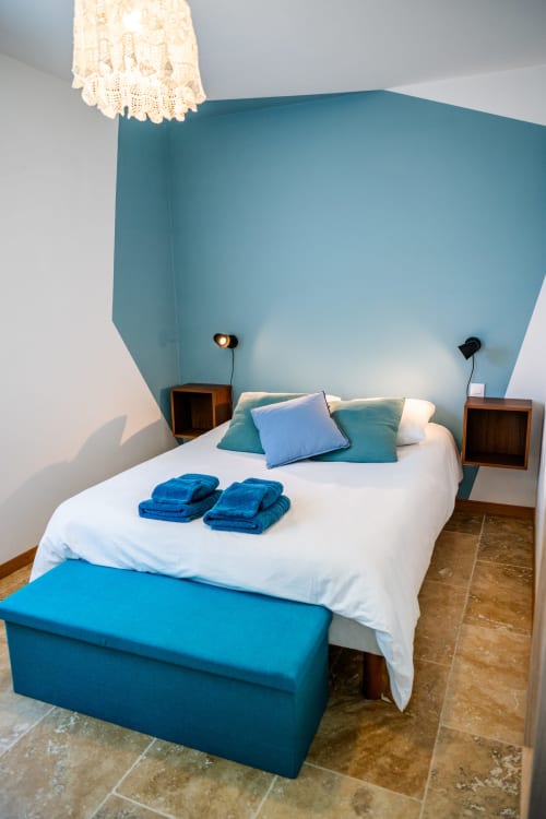 Chambre moderne avec mur d'accent bleu-vert, lit blanc, oreillers bleus et banquette à La Maison Du Saule, Faverolles sur Cher