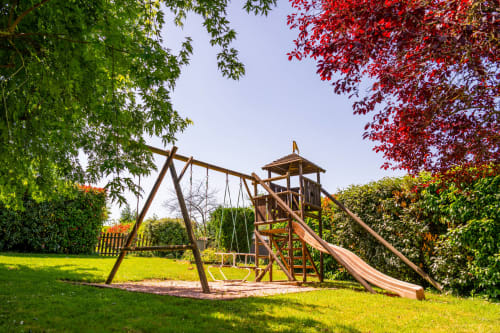 Aire de jeux en bois avec balançoire et toboggan dans le jardin de La Maison Du Saule, Faverolles sur Cher, entourée de pelouse verte
