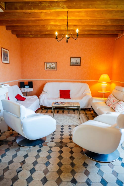 Élégant séjour de la maison du Saule avec murs orangés, mobilier blanc et carrelage géométrique à Faverolles