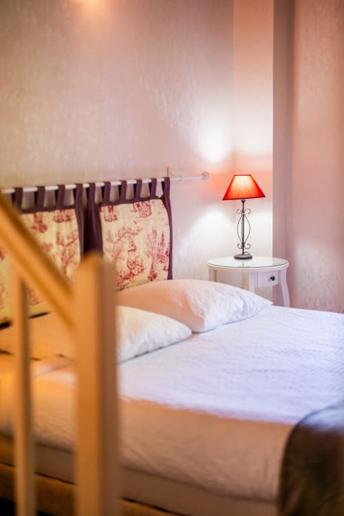Chambre chaleureuse à La Maison Du Saule avec oreillers blancs, rideaux fleuris rouges et lampe de table rouge