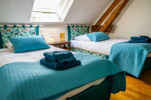Chambre lumineuse sous les combles à La Maison Du Saule avec trois lits, parure turquoise, têtes de lit fleuries et puits de lumière