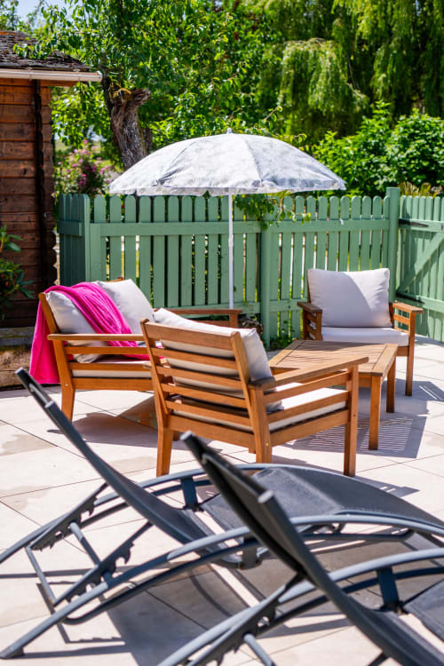 Terrasse ensoleillée de la Maison Du Saule avec transats en bois, parasol blanc et clôture verte à Faverolles-sur
