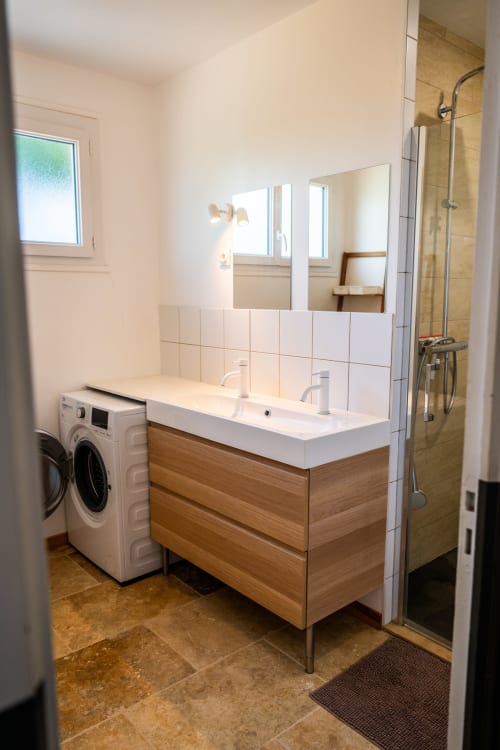 Salle de bains moderne du cottage Petit Saule à La Maison Du Saule avec double vasque, meuble en bois, carrelage blanc et lave-linge