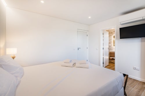 Quarto moderno no apartamento Atlantic Places Salgados Hideaway em Albufeira com roupa de cama branca, TV de parede e jardim