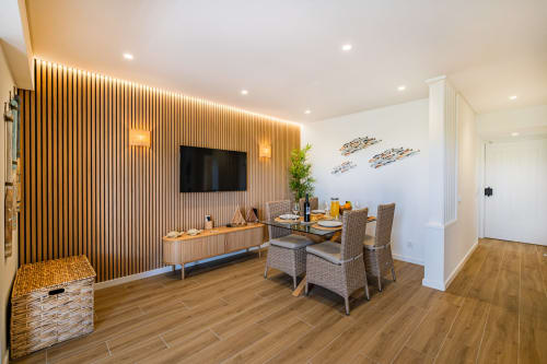 Sala de estar moderna em Atlantic Places Albufeira com parede de TV em painéis de madeira, mesa de jantar e vista para o jardim