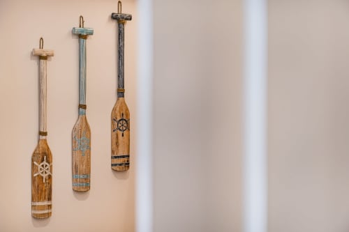 Três remos de madeira náuticos com desenhos de leme de navio e detalhes de corda pendurados na parede bege do Atlantic Places Albufeira