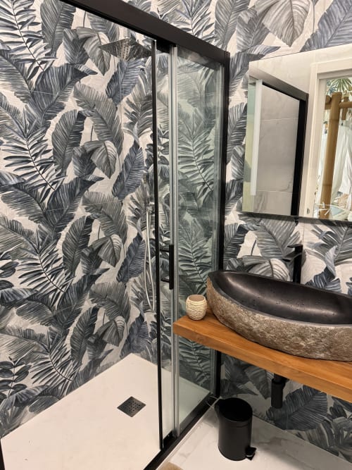 Bagno moderno a Zappy Domus con carta da parati a foglie tropicali, box doccia con cornice nera e lavabo in pietra su legno