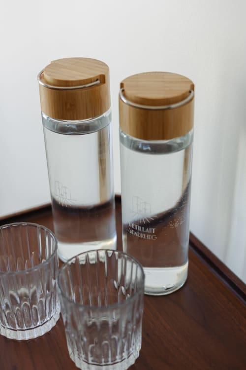Deux bouteilles d'eau à bouchon bambou et verres texturés sur table en bois à L'Ode à Pierre, Dax