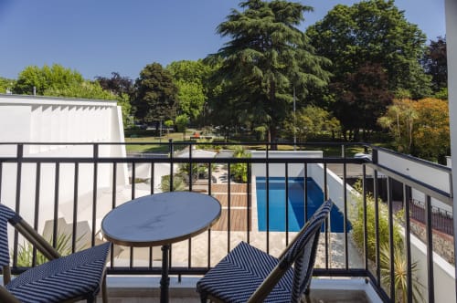 Vue depuis le balcon de L'Ode à Pierre à Dax avec piscine, chaises longues et arbres du parc