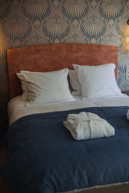 Chambre à L'Ode à Pierre B&B à Dax avec tête de lit rouille, oreillers blancs, literie bleu marine et papier peint à motifs de coquillages