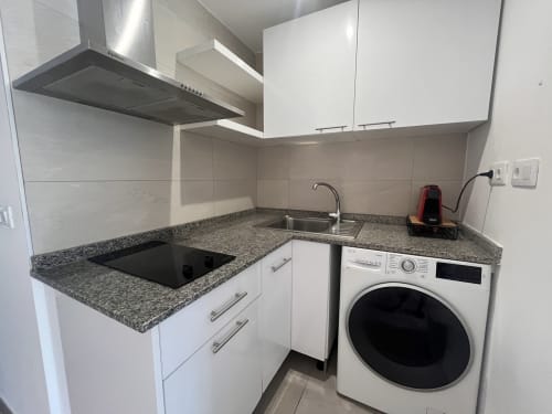 Cocina moderna con encimera de granito, muebles blancos, vitrocerámica, fregadero y lavadora en FTV Holidays Homes