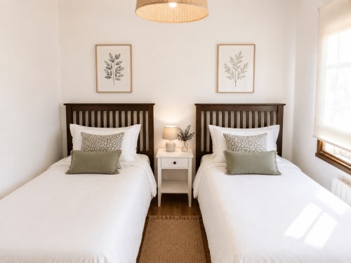Habitación doble del hotel Holibai en Baiona con ropa de cama blanca, almohadas verdes, cabeceros de madera oscura y arte botánico en las paredes.