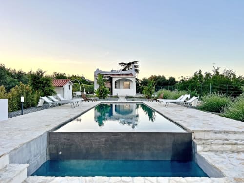 Piscina della villa di lusso Pietra & Luce a Ostuni con lettini, architettura moderna e giardini curati al tramonto
