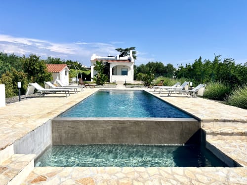 Villa di lusso con piscina a Ostuni, architettura mediterranea, lettini e giardini rigogliosi sotto cielo azzurro