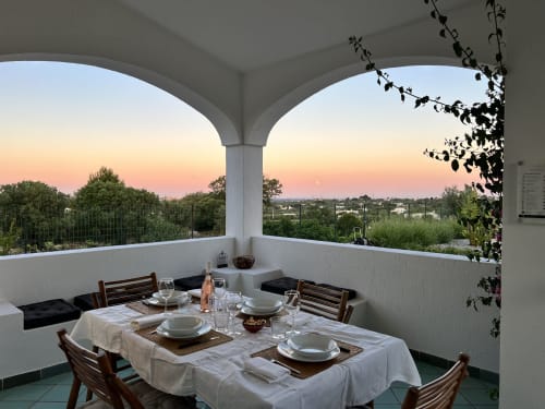 Elegante tavolo da pranzo sulla terrazza coperta della villa Pietra & Luce a Ostuni, con vista sul tramonto e la campagna circostante