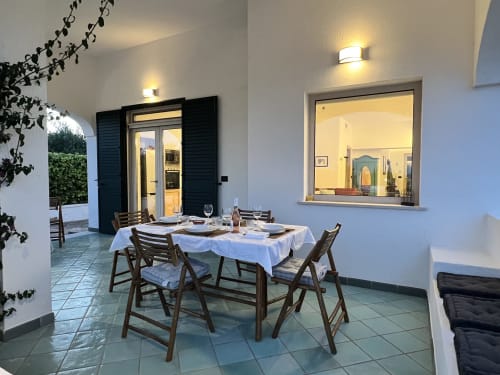 Elegante sala da pranzo della villa Pietra & Luce a Ostuni con tovaglia bianca, sedie in legno e vista aperta sulla cucina
