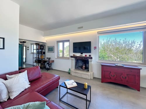 Soggiorno moderno alla villa Pietra & Luce a Ostuni con divano rosso, TV schermo piatto, camino e vista sul giardino