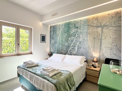 Camera da letto moderna della villa Pietra & Luce a Ostuni con biancheria bianca, murale naturalistico, comodini in legno e vista sul giardino
