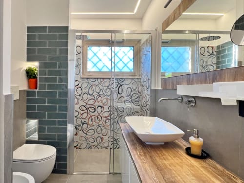 Bagno moderno nella villa Pietra & Luce di Ostuni con parete in piastrelle turchesi, doccia decorata, mobile lavabo in legno e finiture bianche
