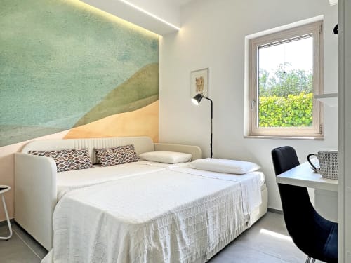 Camera moderna nella villa Pietra & Luce di Ostuni con letto color crema, arte geometrica murale, scrivania e vista sul giardino
